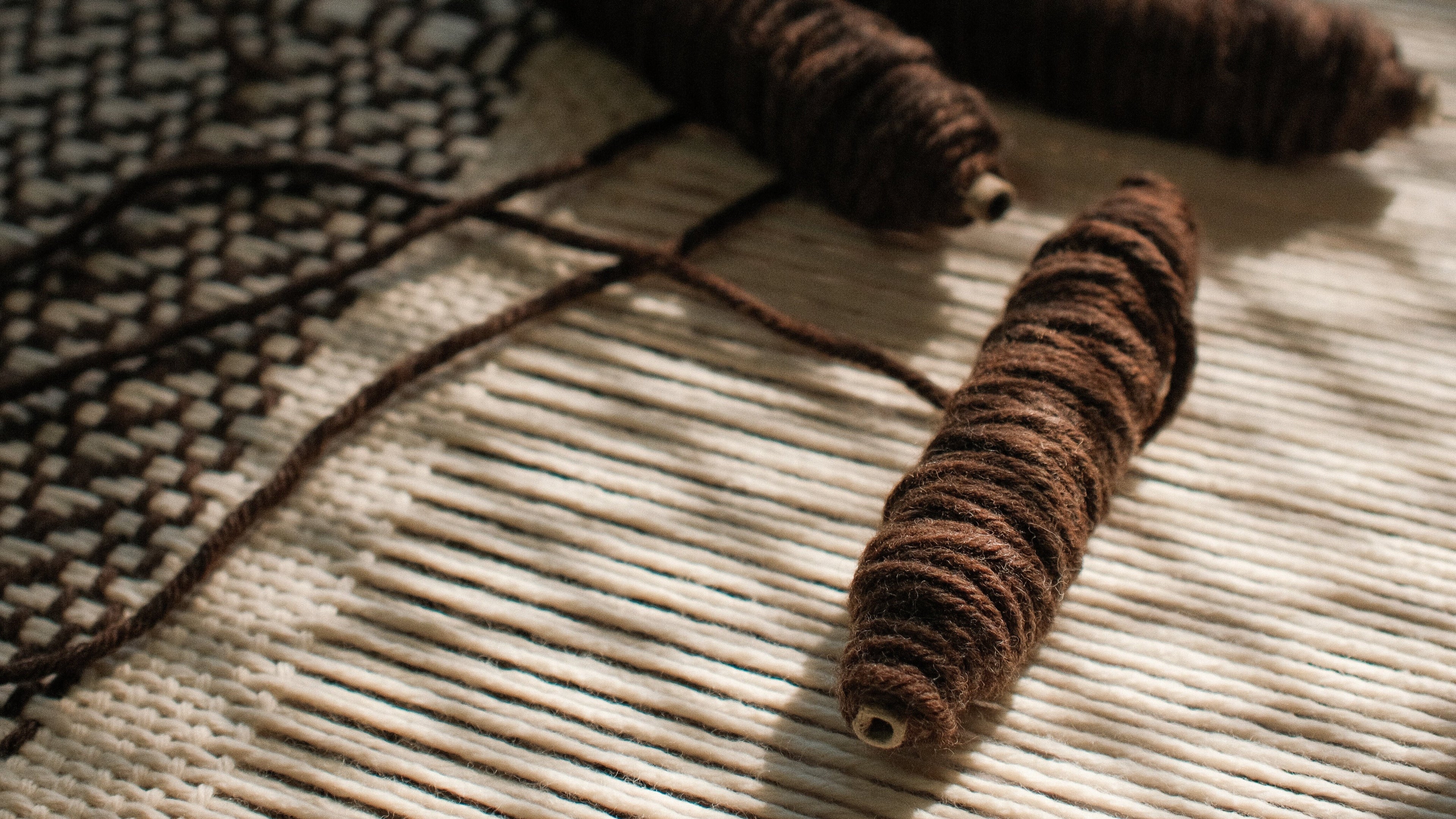 Close-up of hand-spun brown wool yarn resting on a loom, showing the texture and detail of handcrafted weaving by Texturable.