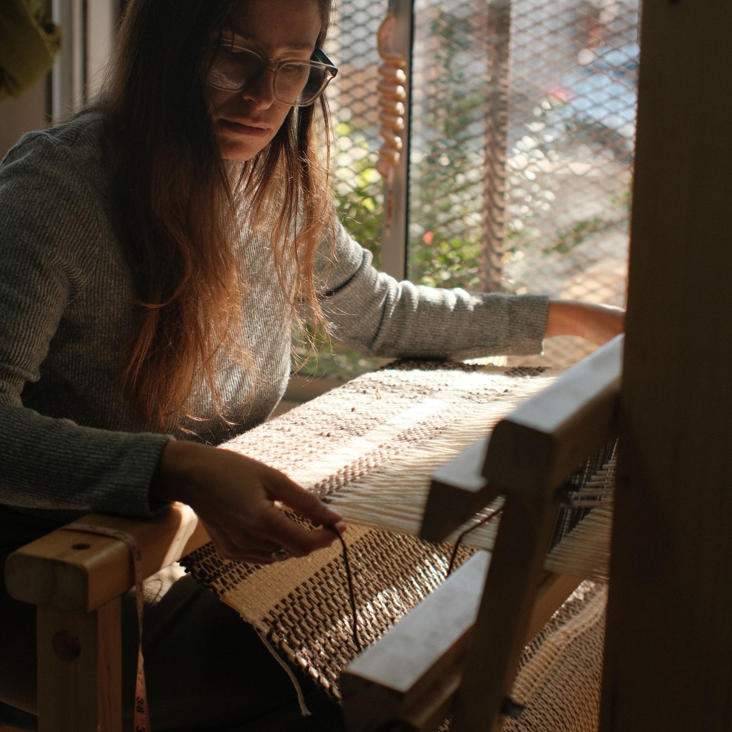 Woman artisan weaving a wool textile on a wooden loom, bathed in warm natural light — handcrafted process by Texturable.