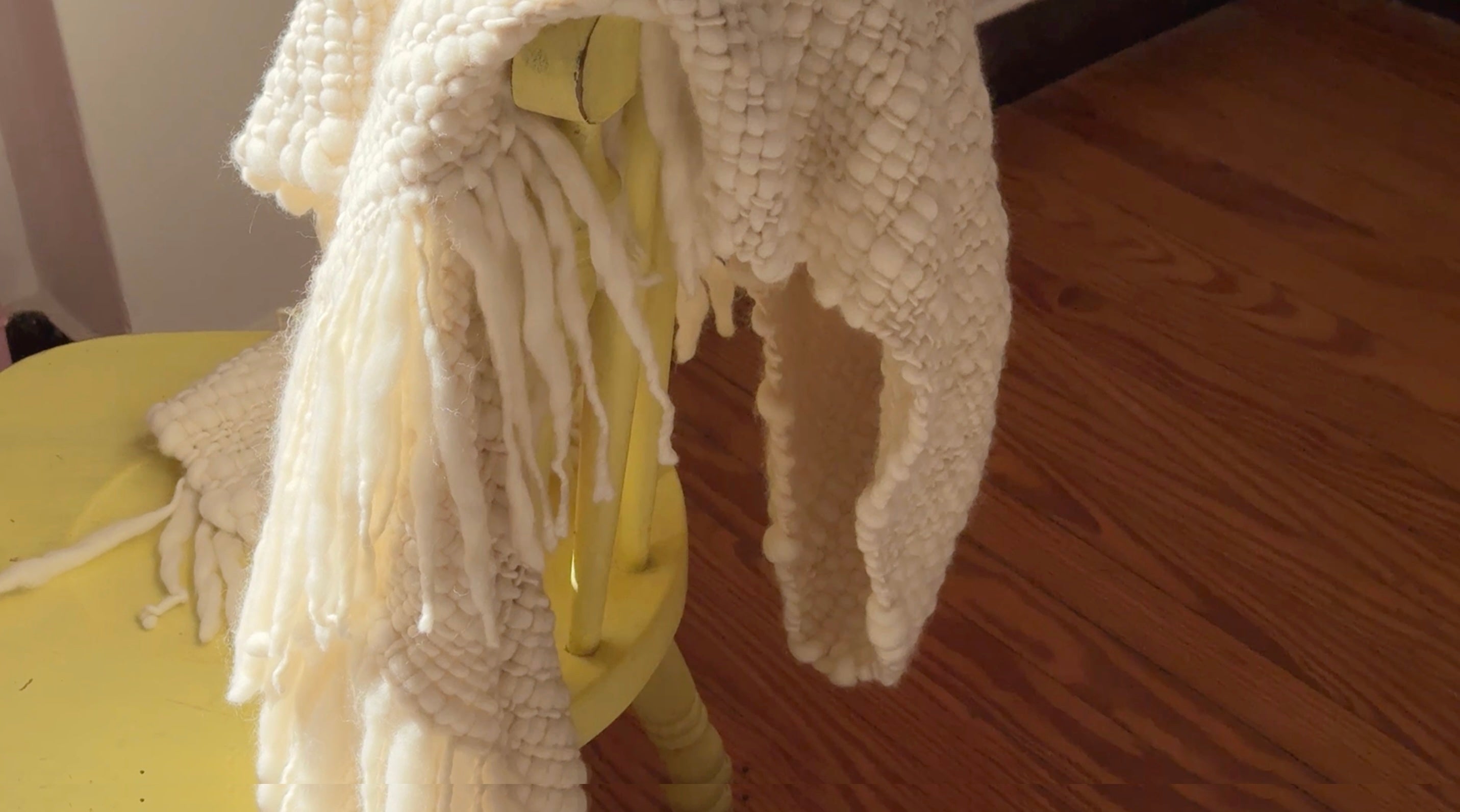 Handwoven wool throw with rich texture draped on a yellow chair, crafted slowly with natural materials.