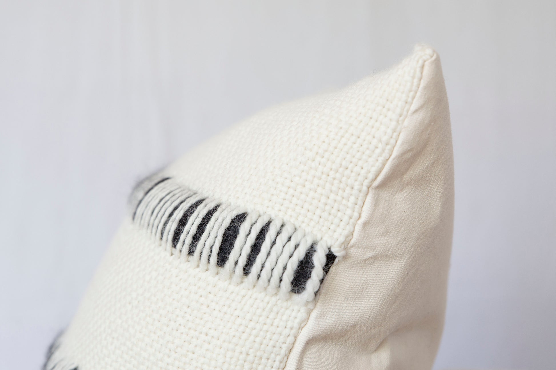Both sides of pillow cover handwoven in merino wool with roving stripes in front and organic cotton at the back - close shot corner